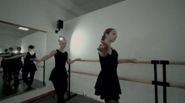 Siyah mayo giymiş genç balerinler bale barre ve ayna koridora bu yansıması yakınında dans vardır. Dans öğretmeni balerinler nasıl düzgün hareketler yapmak kontrol.