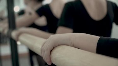 Siyah takım elbiseli küçük balerinlerin ellerine yakın. Bale barını tutan ellerin yakın çekimi
