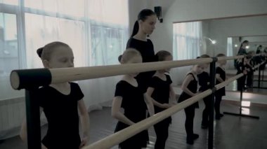 Dans sınıfının sıkı kadın öğretmen bale barre yakın bazı movenments genç öğrenci öğretir, balleres dans ve arka planda yapmak triyes diğer küçük kızlar öğrenmek istiyor