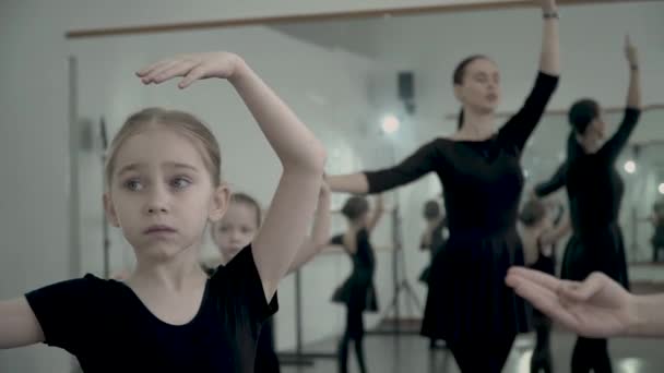 La pequeña bailarina rubia europea vestida de maillot negro hace movimiento de ballet con la maestra y otras chicas todas juntas . — Vídeos de Stock