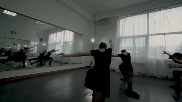 Backside view motion along Ballerinas dressed in black leotards demonstrate ballet movement altogether. — Stock Video