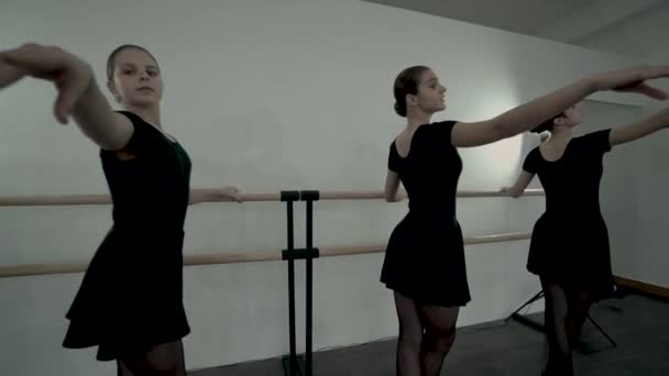 Náctiletých baletky, oblečených v černých leotových tanků, tančí nedaleko baletu. Baletní hodiny. Hladké baletní pohyby na baletní Barre. — Stock video