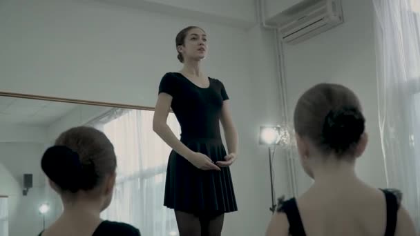 Vista desde atrás de las cabezas de las pequeñas bailarinas que admiran a la hermosa bailarina adulta. Littel balerinas están sentadas en el suelo y mira a la mujer adulta balerina que muestra un nuevo movimiento de ballet . — Vídeos de Stock