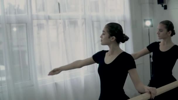 Подростковые балерины, одетые в черные трико, танцуют возле балетной стойки и окна. Балерина делает гладкие движения рук . — стоковое видео