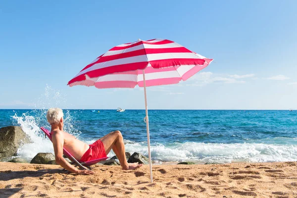 Hombre Mayor Tomando Sol Playa Bajo Sombrilla Con Olas Mar —  Fotos de Stock