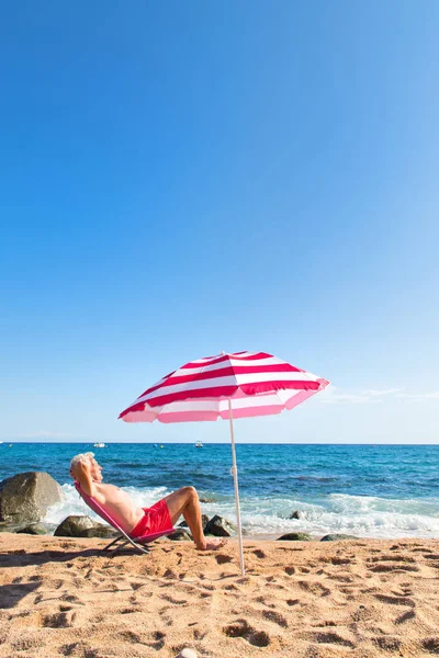 Hombre Mayor Tomando Sol Playa Bajo Sombrilla Con Olas Mar —  Fotos de Stock