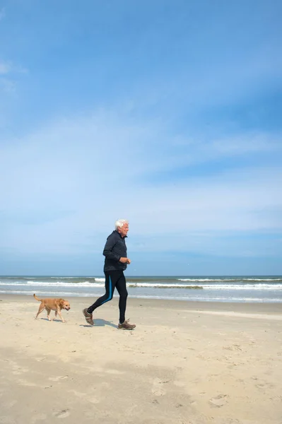 Senior man sporting with dog at beach — Stock Photo, Image