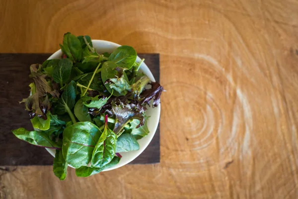 Vegetarian salad from a mix of fresh leaves in a plate on a wooden background