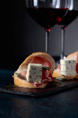 Jambon, mavi peynir ve karanlık bir arka plan üzerinde biberiye ile sandviç. Lezzetli aperatif ve bardak kırmızı şarap. Metniniz için kopya alanı