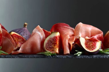 Prosciutto incir ve biberiye karanlık bir arka plan üzerinde.
