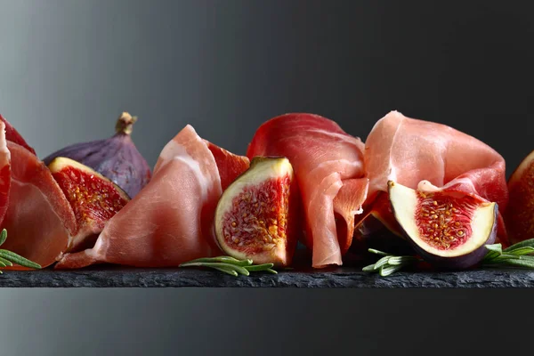 Prosciutto with figs and rosemary on a dark background.