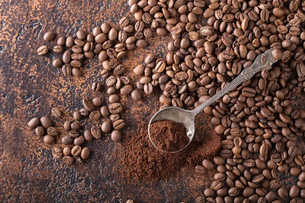 Black roasted coffee grains and ground coffee in spoon lie on a copper table, background image, top view, copy space for your text.