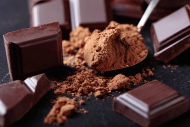 Kırık çikolata parçaları ve siyah arka plan üzerine kakao tozu.