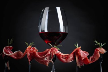 Prosciutto biberiye ve siyah bir zemin üzerine kırmızı şarap ile. Metniniz için kopya alanı.