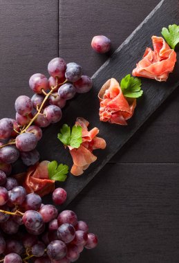 Prosciutto maydanoz ve üzüm siyah bir tablo ile. Üstten görünüm, kopya alanı. 