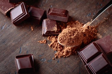 Kırık çikolata parçaları ve ahşap arka plan üzerinde küçük kaşık kakao tozu.