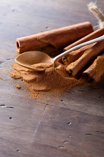 Spoon with cinnamon powder and cinnamon sticks  on a old wooden table.