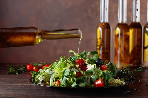 Vegetable salad with olive oil pouring from a small bottle. Old wooden table and brown background.