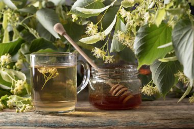 Bardak ıhlamur çayı ile bal ve ahşap masaya çiçek.