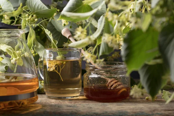 Bardak ıhlamur çayı ile bal ve ahşap masaya çiçek.