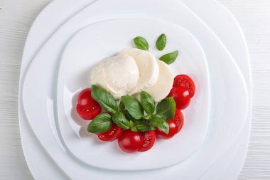 Beyaz tabakta domates ve yeşil Fesleğenli Mozzarella peyniri. Sağlıklı organik gıda.