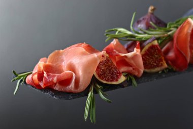 Prosciutto incir ve biberiye karanlık bir arka plan üzerinde.