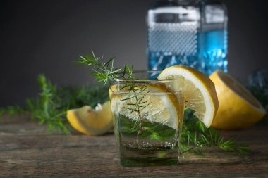Cin, tonik ve limon dilimleri üzerinde eski bir ahşap masa mavi. Alkollü kokteyl limon dilimleri ve ardıç şube ile.