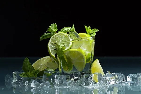 Cocktail with lime , ice  and peppermint leaves on a glass table in bar. Black background .