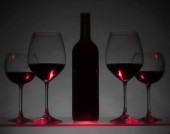 Sklenice a láhev červeného vína na tmavém pozadí.