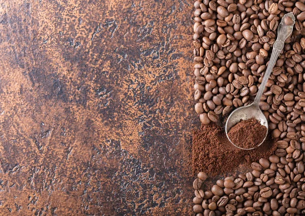 Black roasted coffee grains and ground coffee in spoon lie on a copper table, background image, top view, copy space for your text.