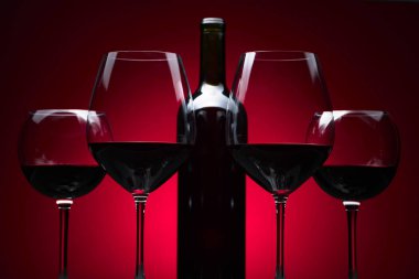 Gözlük ve kırmızı bir arka plan üzerinde kırmızı şarap şişe.