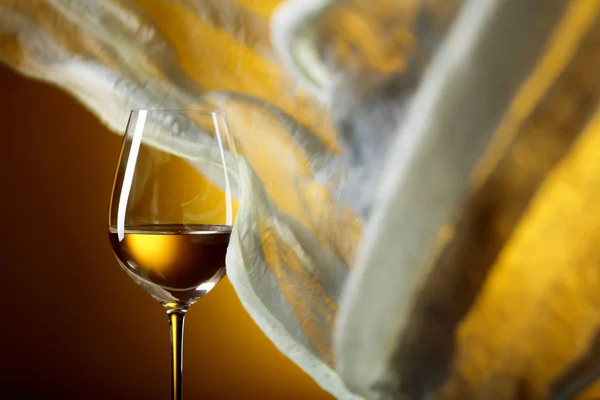 Glass of white wine on a yellow background. Yellow sheer fabric flutters in the wind. Copy space.