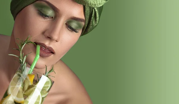 stock image Portrait of a young woman in a green turban with a cocktail of lemon and lime with a branch of rosemary. Copy space.