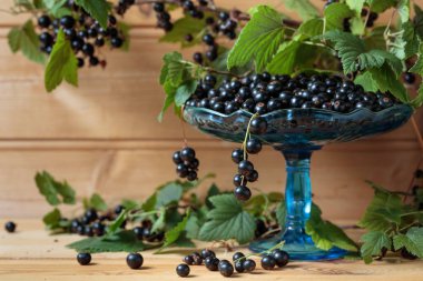 Taze Olgun siyah kuş üzümü rustik ahşap zemin üzerinde. Yeşil yaprakları, yeni berry hasat ile doğal organik çilek ile kase.