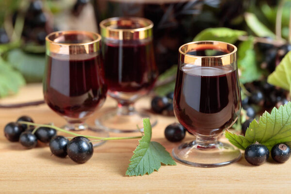 Homemade black currant liqueur and fresh berries on a branch , wooden background.