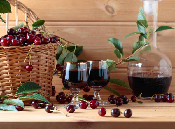 Cherry wine or liquor on wooden background and ripe juicy cherries in basket.