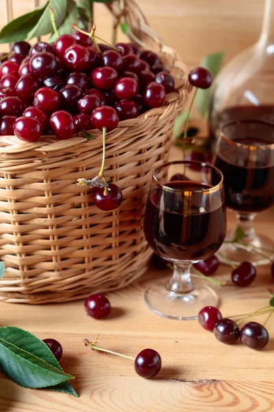 Cherry wine or liquor on wooden background and ripe juicy cherries in basket.