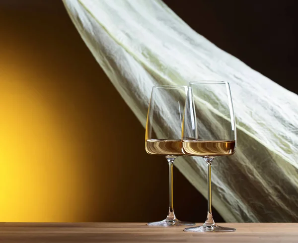 Glasses of white wine on a yellow background. Copy space.  Yellow sheer fabric flutters in the wind. Copy space.