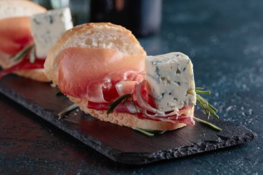 Jambon, mavi peynir ve karanlık bir arka plan üzerinde biberiye ile sandviç. 