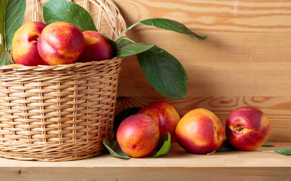 Nectarines with leaves in a wicker basket on a wooden table.