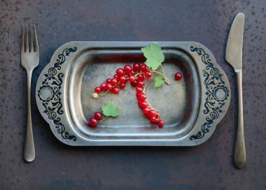 Metal çanak çatal ve bıçak üzerinde kırmızı kuş üzümü. Sağlıklı beslenme, diyet ve antioksidan için kavram. Üstten görünüm.