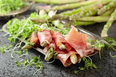 Prosciutto ile tere salatası gri metal arka plan üzerinde sarılı kuşkonmaz.