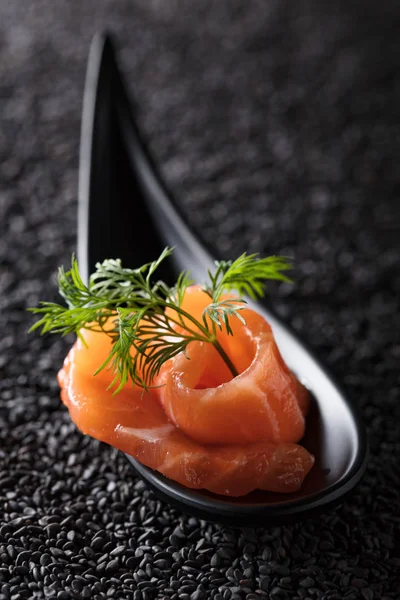 Slice of salted salmon with dill on the background of black sesame.