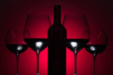 Gözlük ve kırmızı bir arka plan üzerinde kırmızı şarap şişe.