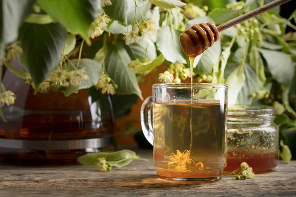 Bardak ıhlamur çayı ile bal ve ahşap masaya çiçek.