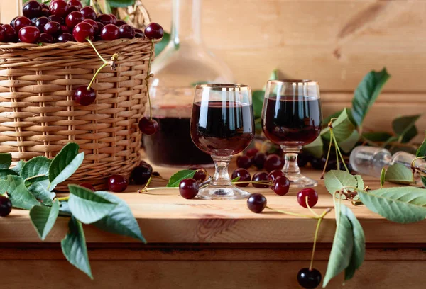 Cherry wine or liquor on wooden background and ripe juicy cherries in basket.