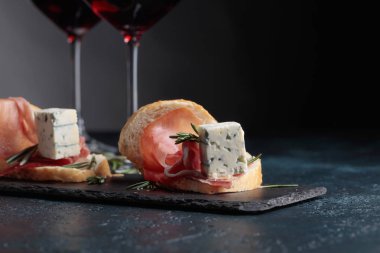 Jambon, mavi peynir ve karanlık bir arka plan üzerinde biberiye ile sandviç. Lezzetli aperatif ve bardak kırmızı şarap. Metniniz için kopya alanı