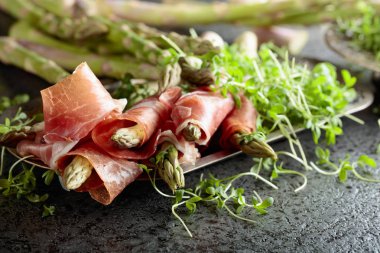 Prosciutto ile tere salatası gri metal arka plan üzerinde sarılı kuşkonmaz.