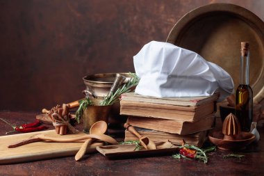 Beyaz şefin şapka ve eski yemek kitapları. Baharat ve mutfak masasında biberiye ile mutfak eşyaları.