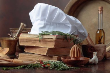 Beyaz şefin şapka ve eski yemek kitapları. Baharat ve mutfak masasında biberiye ile mutfak eşyaları.